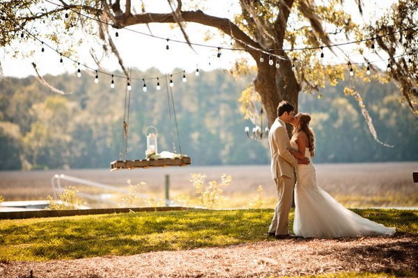 Tara Matt S Southern Wedding On The River Bride And Groom Kissing Under Globe Lights