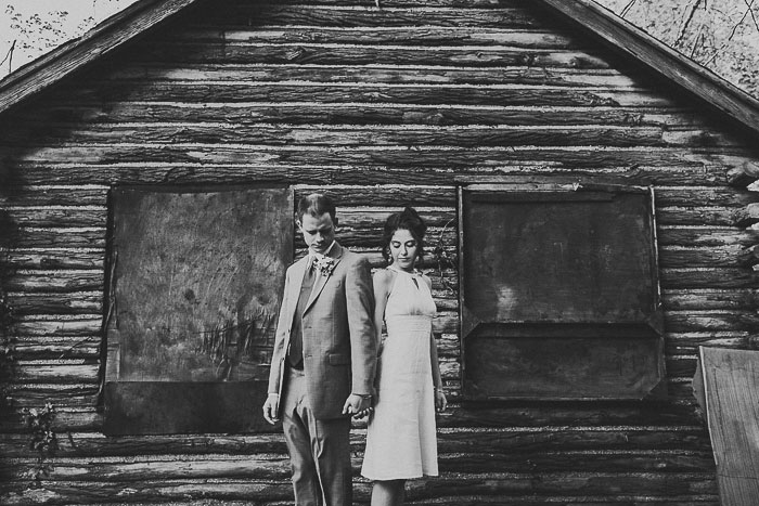 bride and groom in front of abandoned log cabin