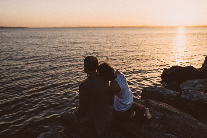 bride and groom sitting by the water at sunset