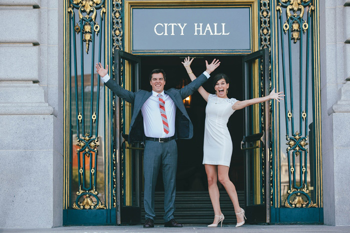 bride and groom jumping for joy outside of city hall