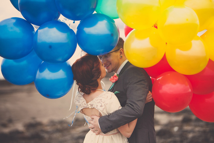 bride and groom kissing beneath balloons