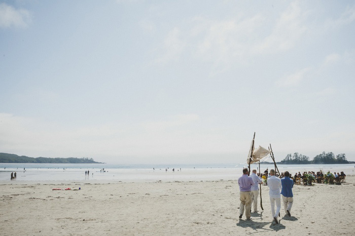 people carrying wedding canopy down the beach