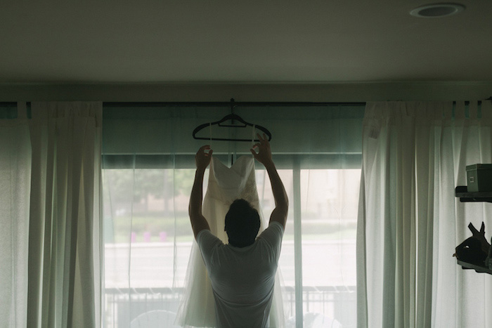 groom hanging up bride's wedding dress