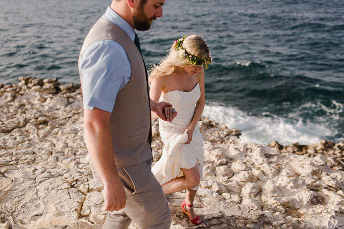 bride holding up her dress walking with groom by the ocean