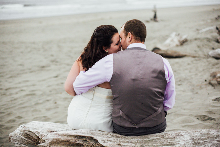 bride and groom sitting on driftwood log