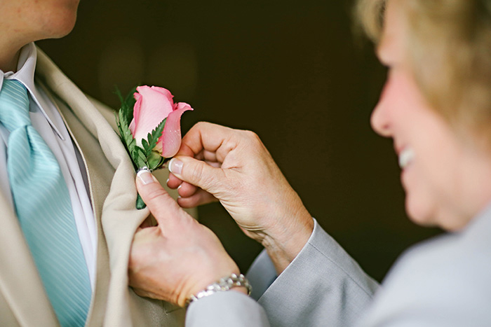 mother pinning pink rose to groom's lapel