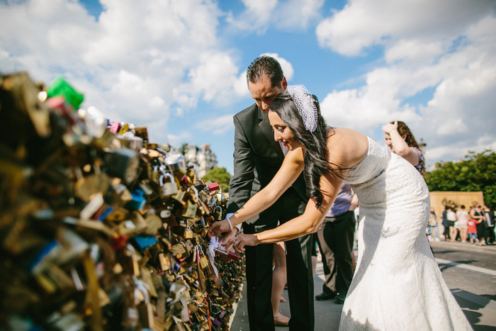 bride and groom adding lock to Paris bridge