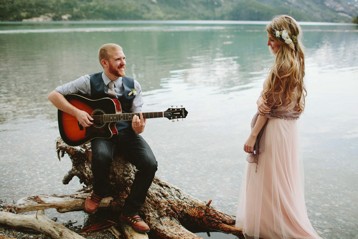 groom playing guitar by the lake