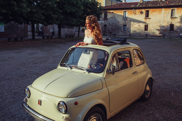 bride standing through sun roof of tiny italian car