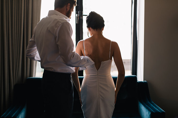 groom zipping up bride's dress