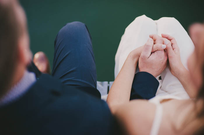 bride and groom holding hands while sitting on the dock