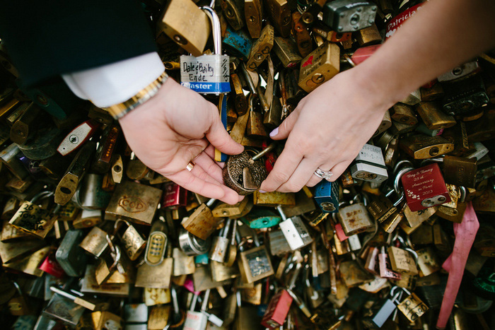 bride and groom putting lock on locks of love bridge