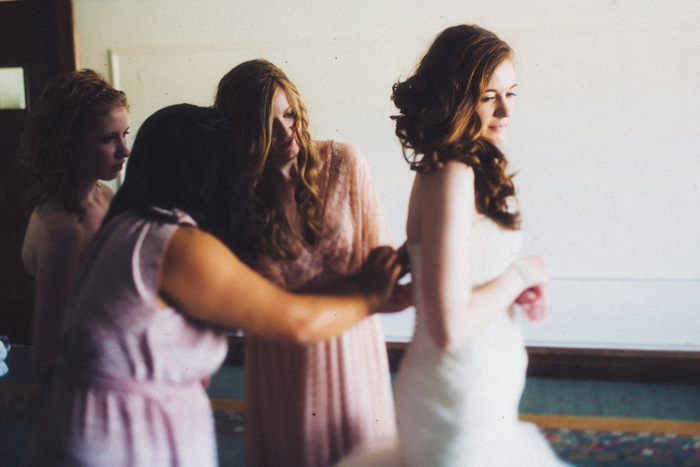 bridesmaids zipping up bride's dress