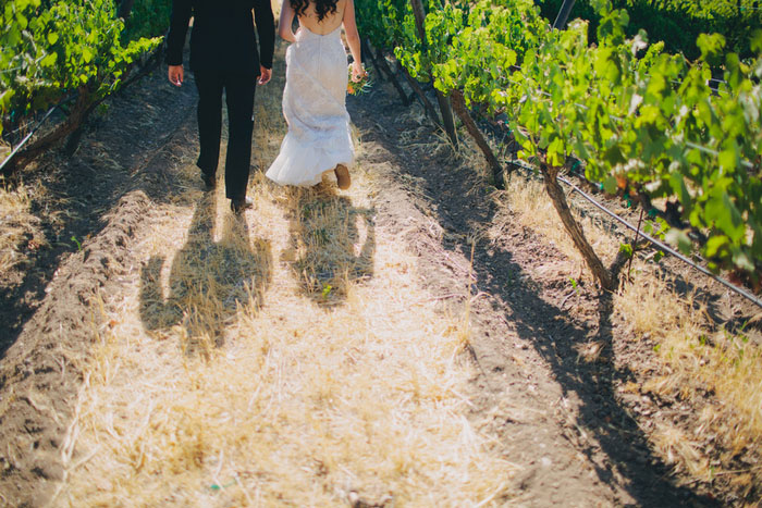 bride and groom walking through vineyard