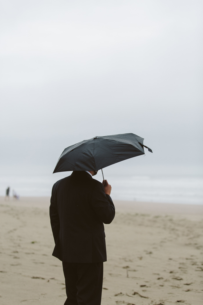 groom on beach under black umbrella