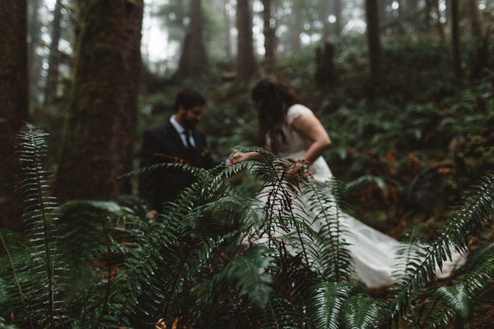 groom helping bride over log in forest