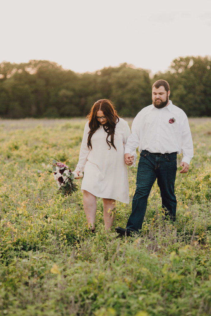 bride and groom walking across field at sunset