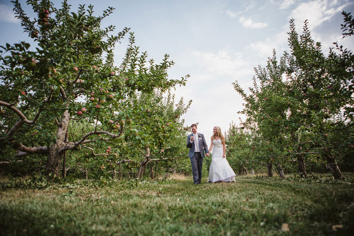 bride and groom walking though apple orchard