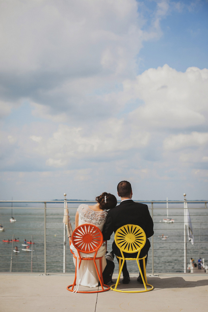 bride and groom sitting by waterfront on colourful chairs