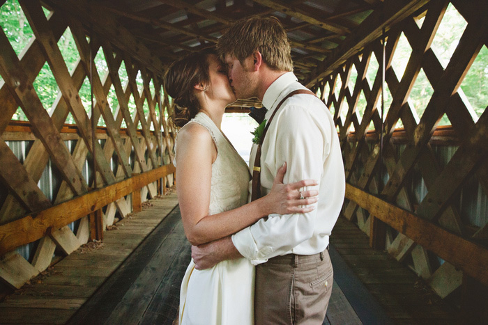 bride and groom kissing on covered bridge