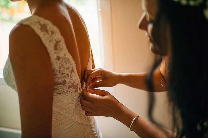 bridesmaid buttoning bride's dress