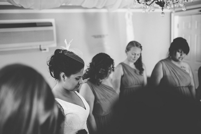 bride holding hands with bridesmaids praying