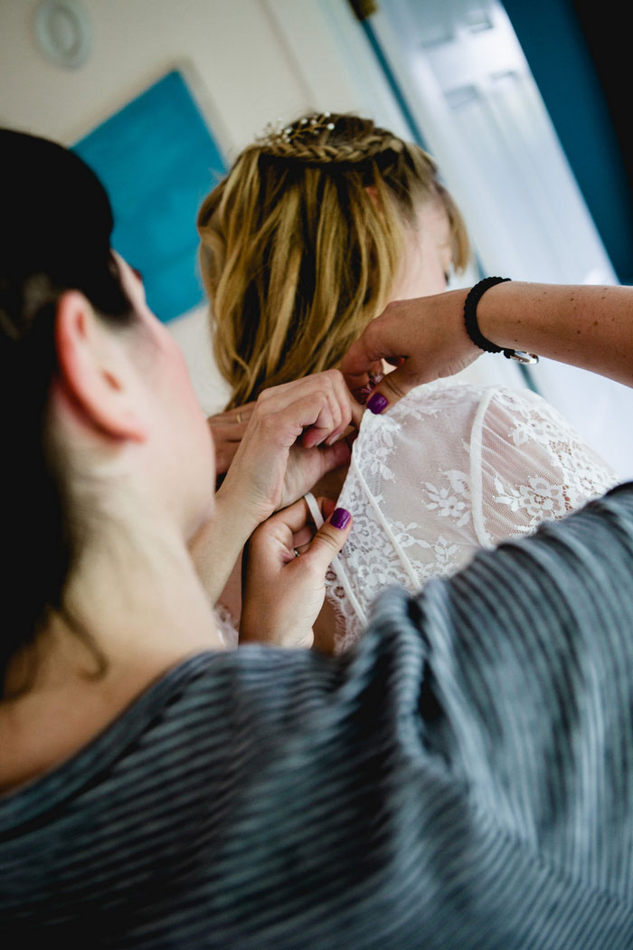 bride getting buttoned into dress