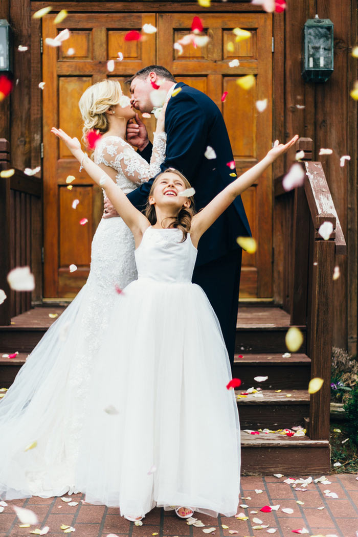 flower girl throwing rose petals as bride and groom kiss