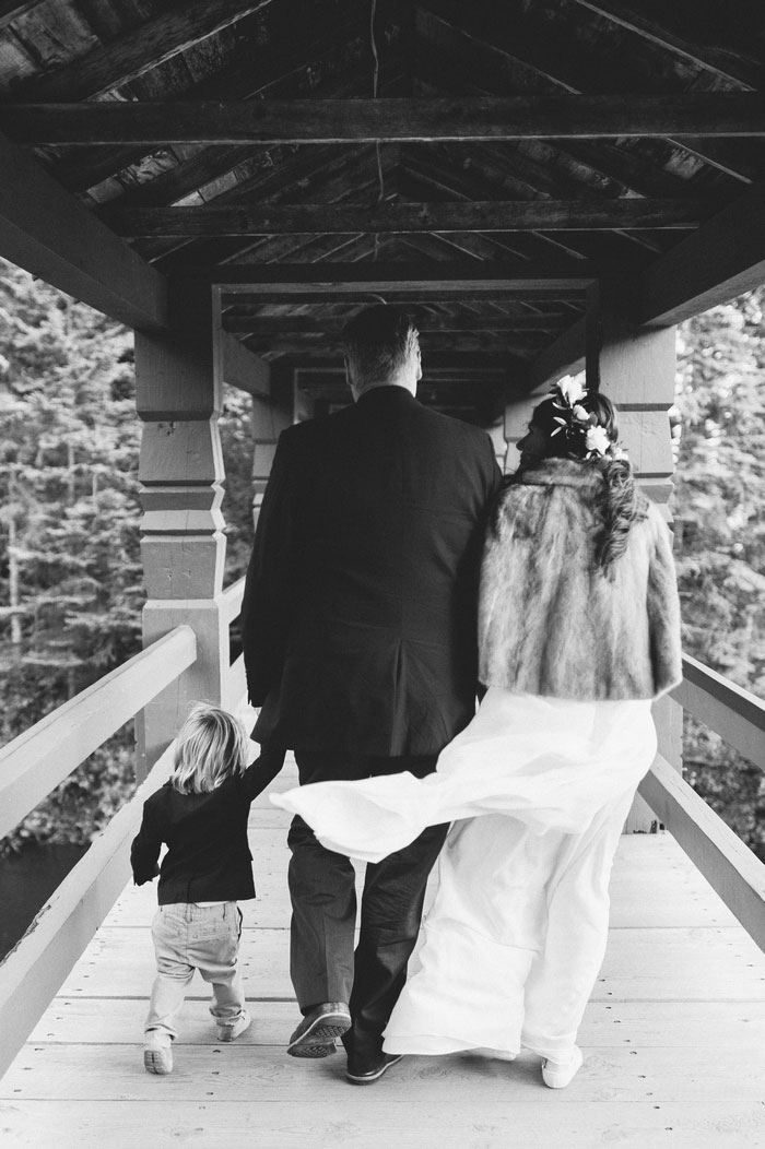 bride, groom, and son walking on covered bridge