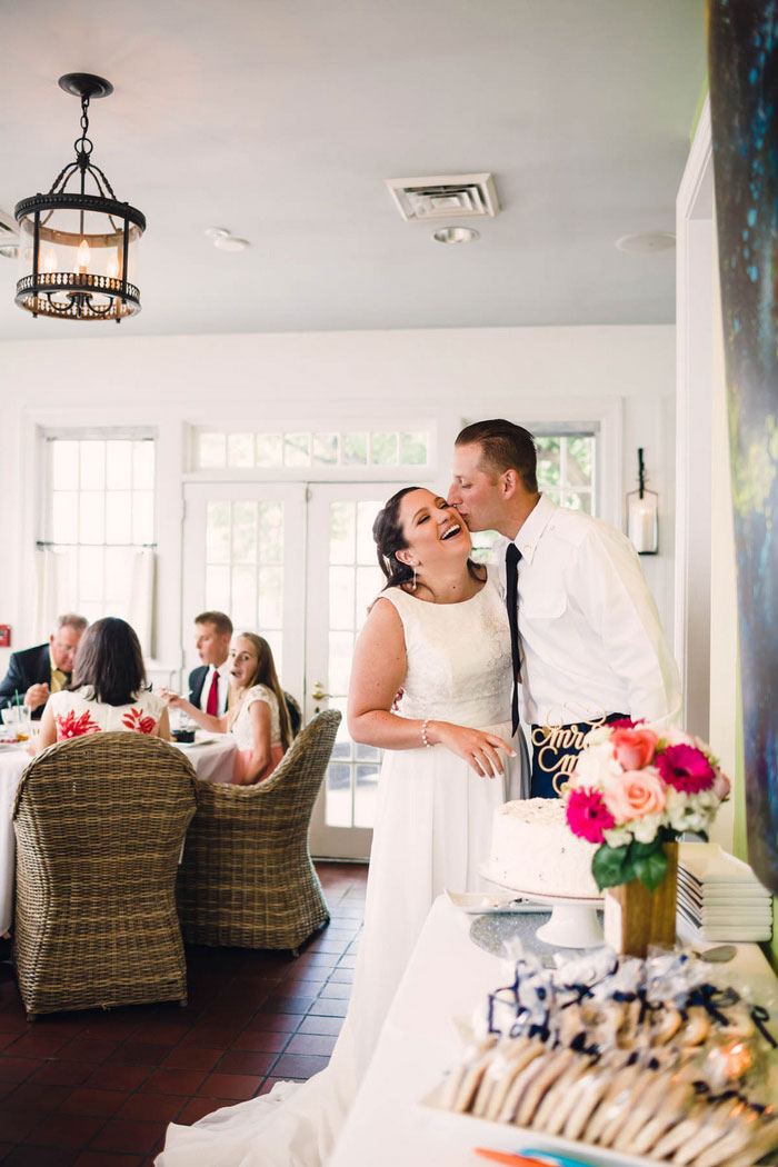 groom kissing bride in front of cake