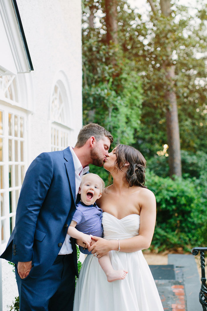 bride and groom kissing while holding baby
