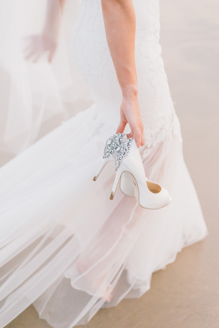 bride carrying shoes on the beach