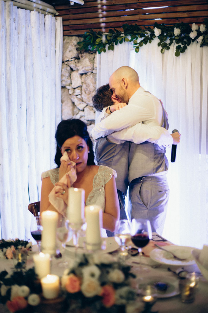 bride wiping away tear as groom and son hug